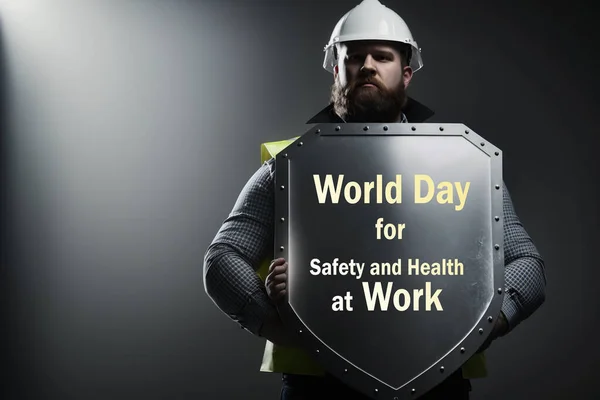World Day for Safety and Health at Work. A worker on a dark background holding a shield. The concept of protecting a worker at work.