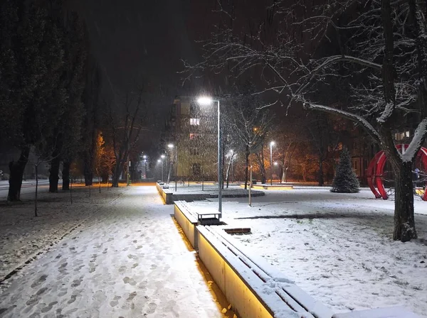 夜は雪に覆われた通りで提灯の光に照らされた黄色いベンチ — ストック写真