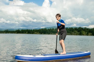 active teen girl paddling a sup board on a river or lake, natural background, active healthy sporty lifestyle. High quality photo