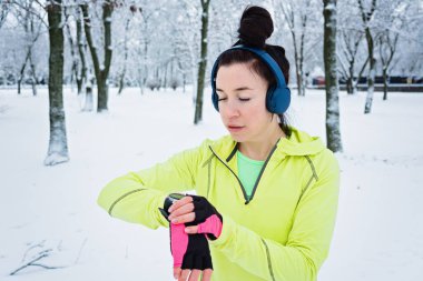 Koşan kadın, kış parkında koşarken kalp atışlarını ve nabzını kontrol ediyor. Fitness kadını kış antrenmanı sırasında koşmak için akıllı saat ayarlıyor..