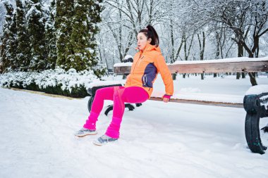 Kış egzersizleri. Kış fitness, soğuk havada egzersiz. Sporcu kadın esneme egzersizleri yapıyor ve karlı kış parkında doğada koşmaya hazırlanıyor.