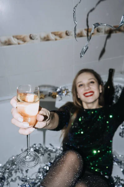 新年庆祝活动 穿着晚礼服的快乐的年轻女人坐在浴缸里 喝着香槟 玩得很开心 — 图库照片
