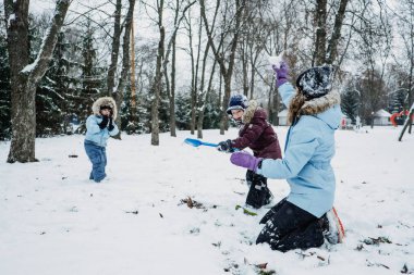 Mutlu Aile, arkadaşlar, anne ve çocuklar kışın karlı arka planda eğleniyorlar. Anne ve iki çocuk dışarıda kış parkında kartopu oynuyorlar. Aile ve arkadaşlar için açık hava kış aktiviteleri