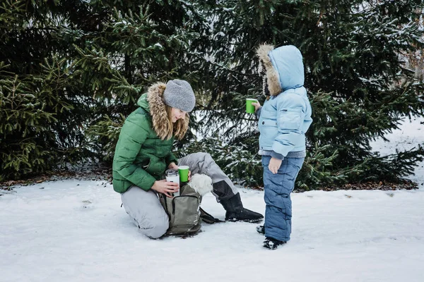 Outdoors winter activities for family. Happy Family, mother, boy kid and dog walking, having fun and drinking hot tea outdoors in winter snowy park nature background