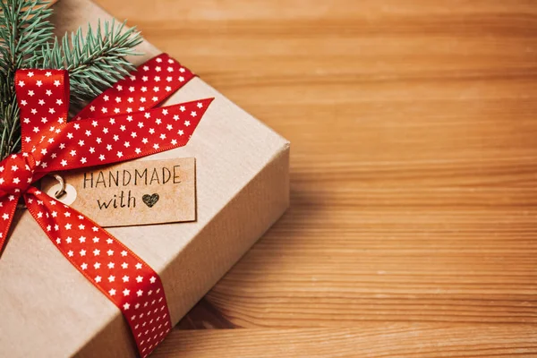 No Gift Christmas Ideas for Family, Friends For An Anti-Consumerist Christmas. Xmas gift kraft paper box with red ribbon, fir-tree and Handmade with love label on wooden table.