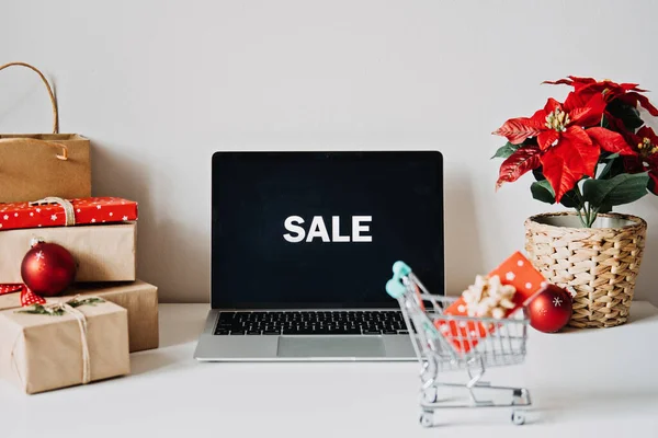 Stock image Open laptop computer with word Sale on Display screen, Poinsettias Christmas Flower and gift boxes on white table. Christmas online shopping, Winter sales