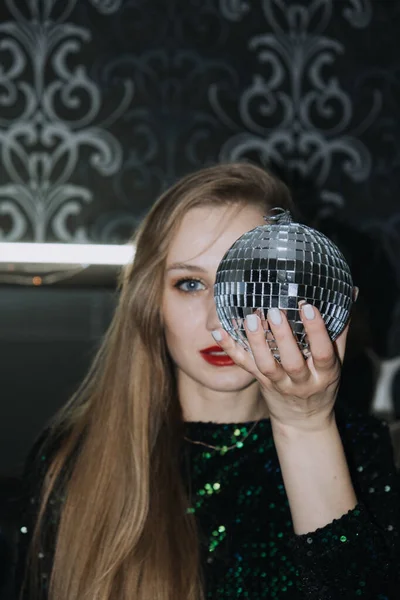 New year eve night club party. Chic image of Beautiful girl in sparkles evening dress with disco ball in hands. Disco style model with mirror ball.