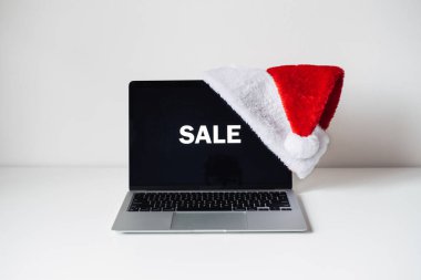 Beyaz masada kelime indirimi ve Noel Baba şapkası olan dizüstü bilgisayarı göster. Bayramlık ofis masası çalışma alanı. Noel alışverişi, kış satışları, Xmas ecommerce.