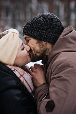 Sevgililer Günü çifti dışarıda. Kış buluşmaları, Takılmak için Buluşma Fikirleri. Çiftler için soğuk sezon buluşmaları. Genç çift kış karlı parkta öpüşüyor ve sarılıyor.