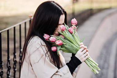 Spring, self love, self care. Candid portrait of happy woman with tulips bouquet outdoors. Beautiful woman walking with bouquet of tulips in city streets.