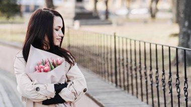 Spring, self love, self care. Candid portrait of happy woman with tulips bouquet outdoors. Beautiful woman walking with bouquet of tulips in city streets.