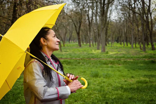 Stress resilience and mental health, concept. Managing stress and building resilience. Happy senior woman in yellow rain coat with yellow umbrella walking in park