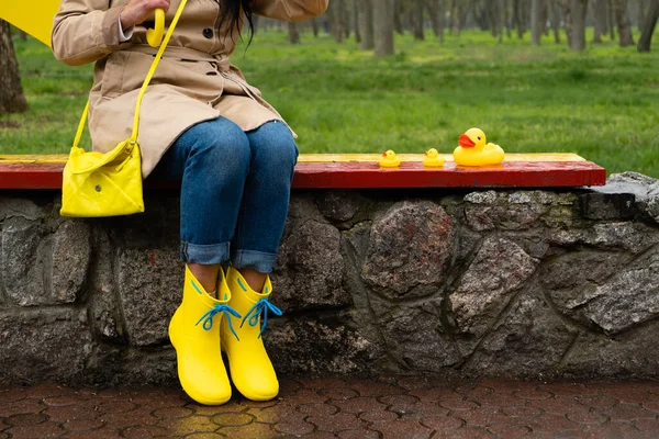 Stress resilience and mental health, no depression concept. Womens legs in yellow rubber boots and a yellow rubber duck in the rain in the park