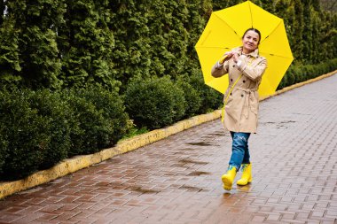Happy senior woman in yellow rain coat with yellow umbrella Encouraging self-care and relaxation, Using the rain as opportunity for reflection and introspection.