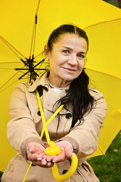Happy senior woman in yellow rain coat with yellow umbrella Encouraging self-care and relaxation, Using the rain as opportunity for reflection and introspection.