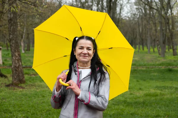 Happy senior woman in yellow rain coat with yellow umbrella Encouraging self-care and relaxation, Using the rain as opportunity for reflection and introspection.