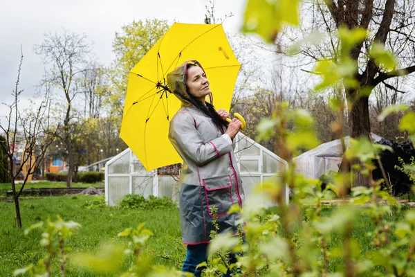 Coping with stress and anxiety. Practicing mindfulness and relaxation techniques. Happy senior woman in yellow rain coat with yellow umbrella walking and enjoying life in rainy park.