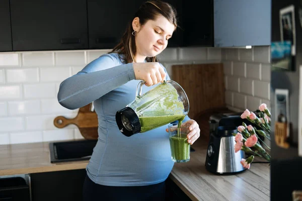 为怀孕和产后 产前营养提供的绿色平滑疗法 怀孕妇女在厨房里用搅拌机和饮料配制绿色维生素冰沙 — 图库照片