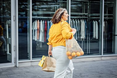 Boyut-kapsayıcı vücut pozitifliği, vücut ölçülerinin ve şekillerinin kabul edilmesi ve kutlanması gerektiğini savunur. Buna kilolu ya da kilolu olmak da dahil. Şehir caddesinde sarı elbiseli mutlu kıvrımlı genç kadın..