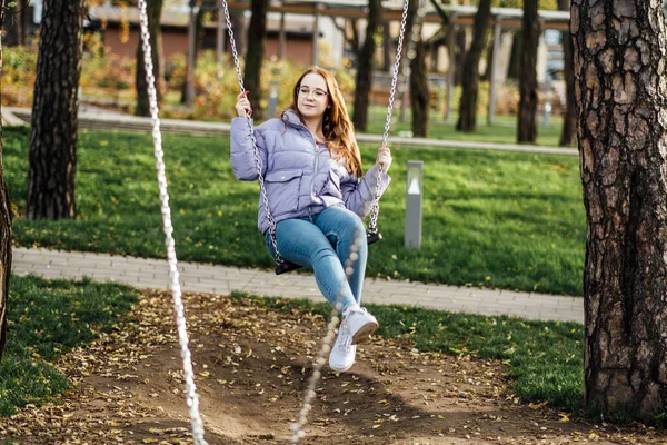 Teens Mood swings: Hormonal changes can cause mood swings, irritability, and emotional outbursts in teenage girls. Teenager girl in glasses on swing in city park