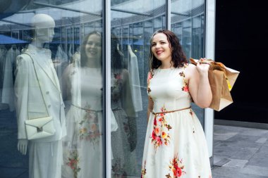 Boyut Çeşitliliğinin Geleceği. Ana cadde, vücut çeşitliliğinde lüks modadan daha iyidir. Büyüklük çeşitliliği eksikliği. Havalı, kıvrımlı, alışveriş torbalı, kilolu bir kadının açık hava portresi.