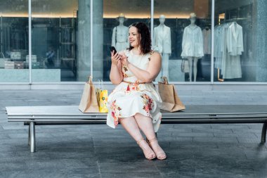 Satış için Al Chatbots, Destek, Ticaret Chatbotları ile Alışveriş. Alışveriş çantalı genç bir kadının açık hava portresi akıllı telefonda sohbet robotu kullanıyor..