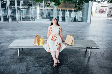 Ruh Sağlığı üzerine alışveriş yapmanın etkileri. Takıntılı Alışveriş Bozukluğunu anlamak. Alışverişkolik kadın, açık hava alışveriş torbalarında birden fazla alışveriş yaptıktan sonra....