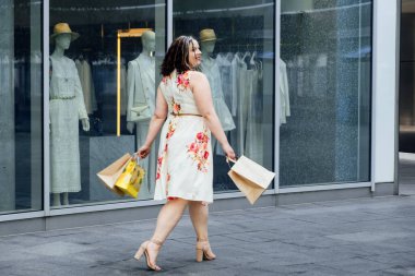 Boyut Çeşitliliğinin Geleceği. Ana cadde, vücut çeşitliliğinde lüks modadan daha iyidir. Büyüklük çeşitliliği eksikliği. Havalı, kıvrımlı, alışveriş torbalı, kilolu bir kadının açık hava portresi.