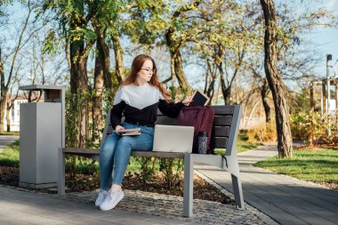 SMART Eğitim ve Öğrenciler İçin Yaşam Hedefleri. Şehir parkında dizüstü bilgisayarı ve sırt çantası olan kızıl saçlı kızın açık hava portresi..