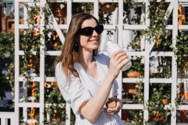 Yaz boyunca vücudun ne kadar suya ihtiyacı olursa, İçmek için kaynaşmış suyu çıkar. Daha fazla su içmek için yaz tavsiyeleri. Güneşli yaz şehrinde elinde su şişesi olan bir kadın..