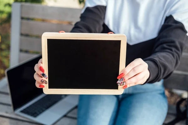 Young student girl holding black chalkboards with blank copy space screen for your advertising text message on laptop outdoor background.