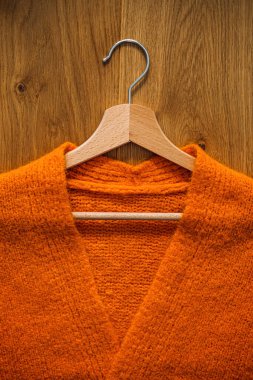 Sonbahar minimalist gardırop, ahşap elbise askısında turuncu, sıcak örülmüş süveter. Sonbahar kapsülü, sıcak moda trendleri ve şık, sıcak arka plan, örgü giysileri, kopyalama alanı