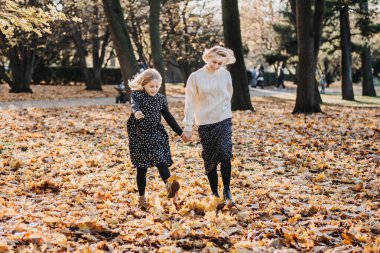 Mutlu sonbaharlar. Gençli aileler için sonbahar sonbahar aktiviteleri. Çocuklar ve Aileler için Sonbaharın tadını çıkarma yolları. Autumn Park 'ta annesiyle yürüyüp oynayan tatlı bir genç kız.