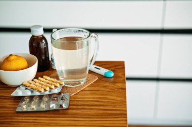 Doğal ve tıbbi soğuk algınlığı ve grip ilaçları evdeki masada. Soğuk algınlığı ve grip sonbahar ve kış mevsimlerinde düşer. Sıcak çay, limon, termometre hapları ve kapsüllü fincan..