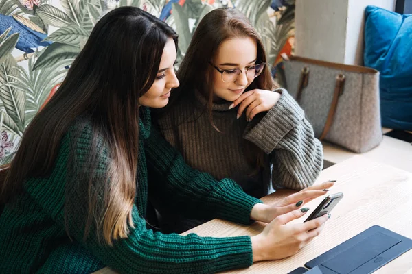 Gen Z influence on the development and popularity of short-form video content on social media platforms. Two girlfriend in cozy sweaters share a moment over smartphone and record video.