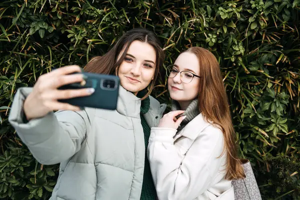 Gen Z influence on the development and popularity of short-form video content on social media platforms. Two girl friends share a moment over smartphone and record video outdoors.