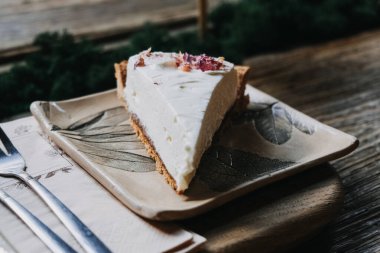 Botanik Seramik Tabakta Kremalı Cheesecake dilimi. Kurumuş yapraklarla kaplı zarif cheesecake dilimi, yaprak desenli seramik tabakta mükemmel sunuluyor.