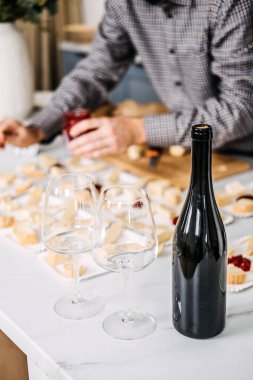 Peynir eşleşmeli şarap tatma hazırlığı. Sommelier şarap tatma etkinliğine hazırlanıyor, çeşitli peynirleri şaraplarla dikkatlice eşleştiriyor, açılmamış bir şişe ve zarif bardaklar sunuyor.