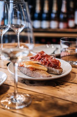 Üzerinde peynir ve pişirilmiş jambon bulunan, ahşap bir masanın üzerinde zarif şarap kadehleri bulunan İspanyol İspanyol tapalarının davetkar bir gösterisi.