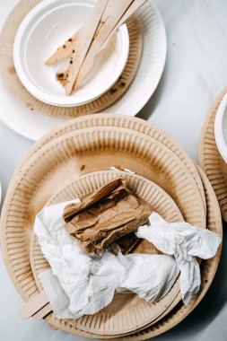 Bir masada biyolojik çözünür tabaklar ve ahşap kaplar kullanılıyor. Tek kullanımlık sofra takımı için çevre dostu seçimi vurgulanıyor..