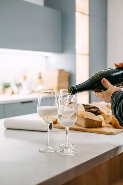 A hand pours sparkling wine into elegant glasses, set against a kitchen backdrop, perfect for an exquisite food and wine pairing.