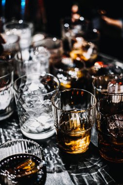 Mükemmel biçimlenmiş bir buz küresi içeren viski kokteylinin yakın çekimi, karamsar, sofistike bir bar atmosferinin ortam aydınlatmasıyla vurgulanır..