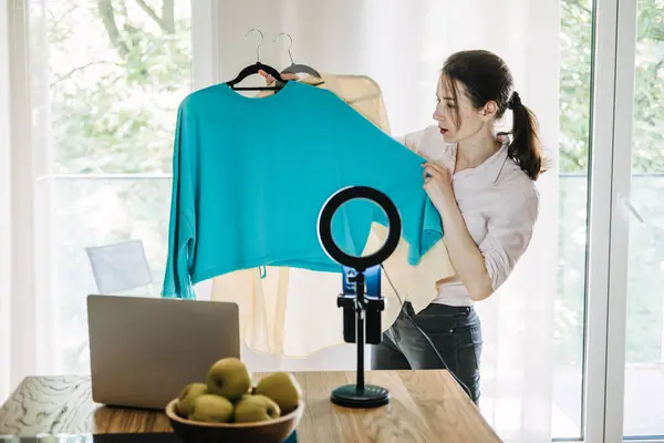 stock image A fashion blogger presenting two outfits during a live stream, using a ring light and laptop, symbolizing content creation, influencer marketing, and online fashion advice.