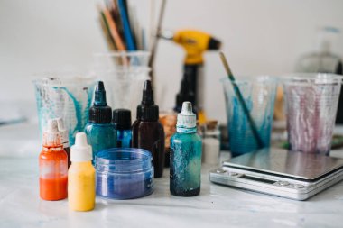 Close-up of colorful resin pigments, cups, and tools spread across a worktable in a creative studio. vibrant color palette and essential supplies used in a DIY epoxy resin art project. clipart