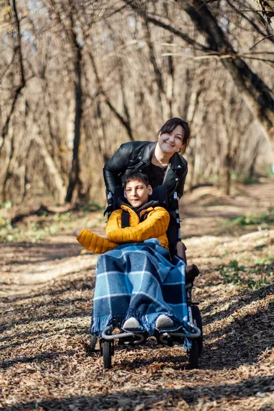 stock image A mother and her child, who is in a wheelchair, share a moment during a nature walk in the forest. The image emphasizes the importance of accessibility in outdoor activities