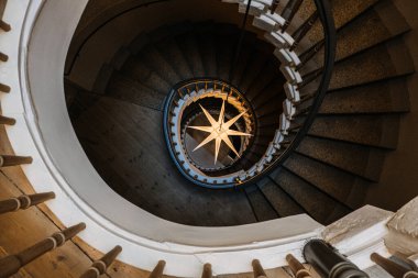 Merkezi yıldız şekilli aydınlatma armatürüne sahip spiral bir merdivenin üstünden, mimari simetri, iç tasarım ve tarihi bir binada soyut desenler gösterilir..