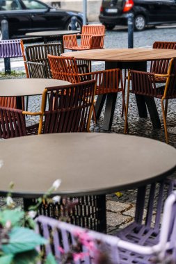 Gölgeli bir verandanın altında boş masaları ve sandalyeleri olan açık bir kafe, tarihi Avrupa mimarisine karşı kurulmuş, rahat bir şehir yemek atmosferi yaratıyor..