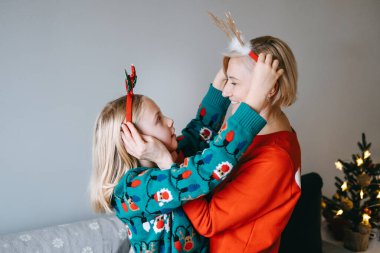 Bir anne ve kız, Noel zamanı aile bağlarının neşe ve sıcaklığını yakalayan, birbirlerine neşeli saç bantları takan neşeli bir anın tadını çıkarırlar..