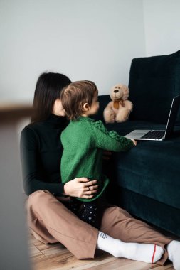 Bir anne, meraklı bebeği işe koyulurken dizüstü bilgisayarıyla çalışır. Aile dostu bir çalışma ortamı ve etkin bir iş hayatı entegrasyonu ihtiyacını gösterir..