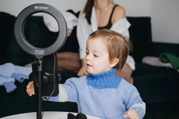 stock image A curious toddler interacts with a ring light during a family video shoot, showcasing behind-the-scenes content creation and child exploration in a digital environment.